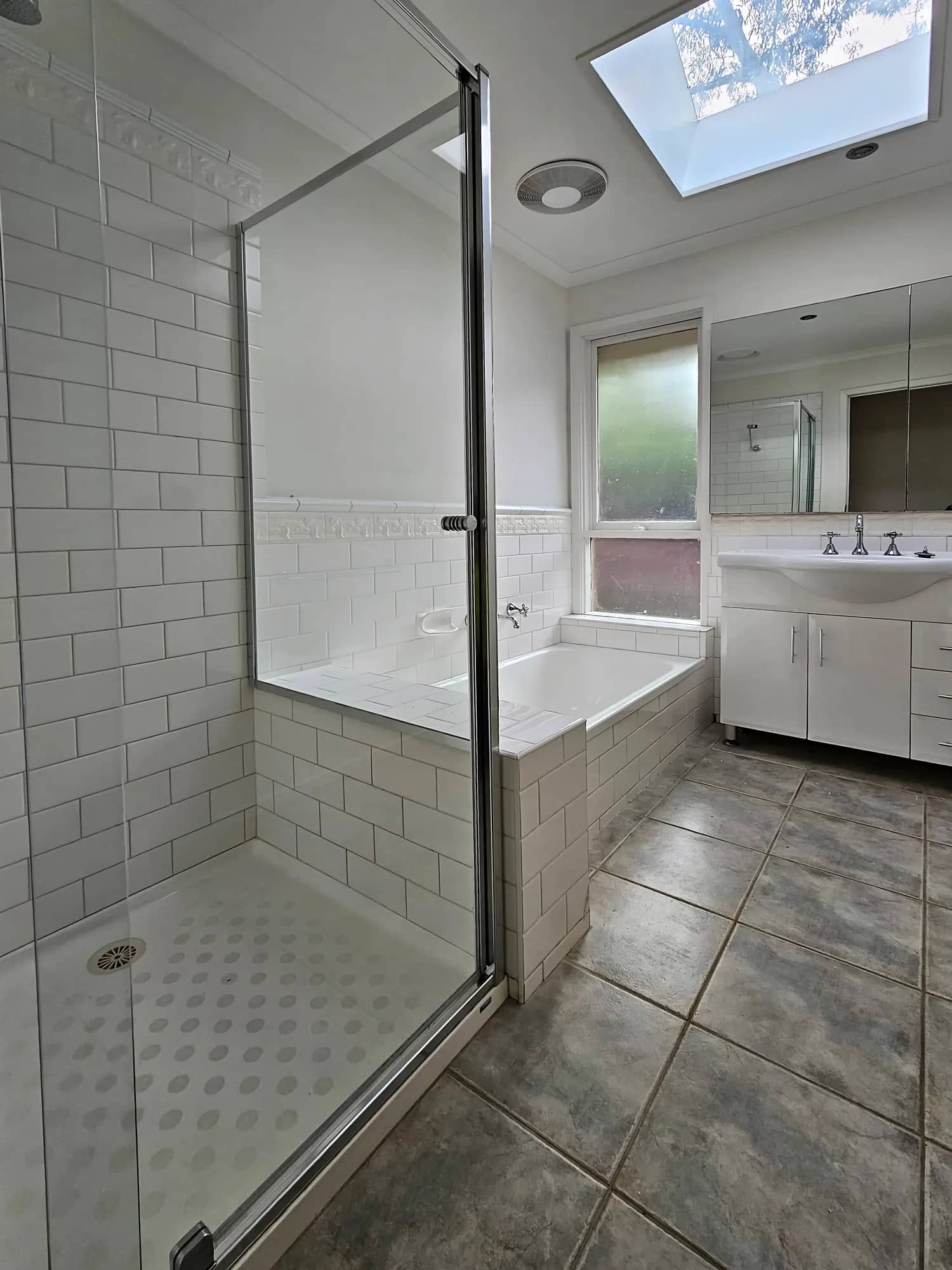 Bathroom with white subway wall tiles, a glass shower screen, dark floor tiles and a skylight