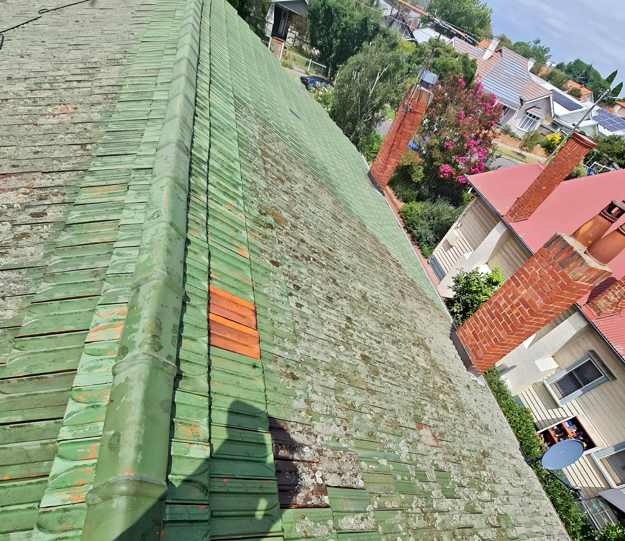 Tile roof with a worn green coating, lichen growth and mismatched replacement tiles