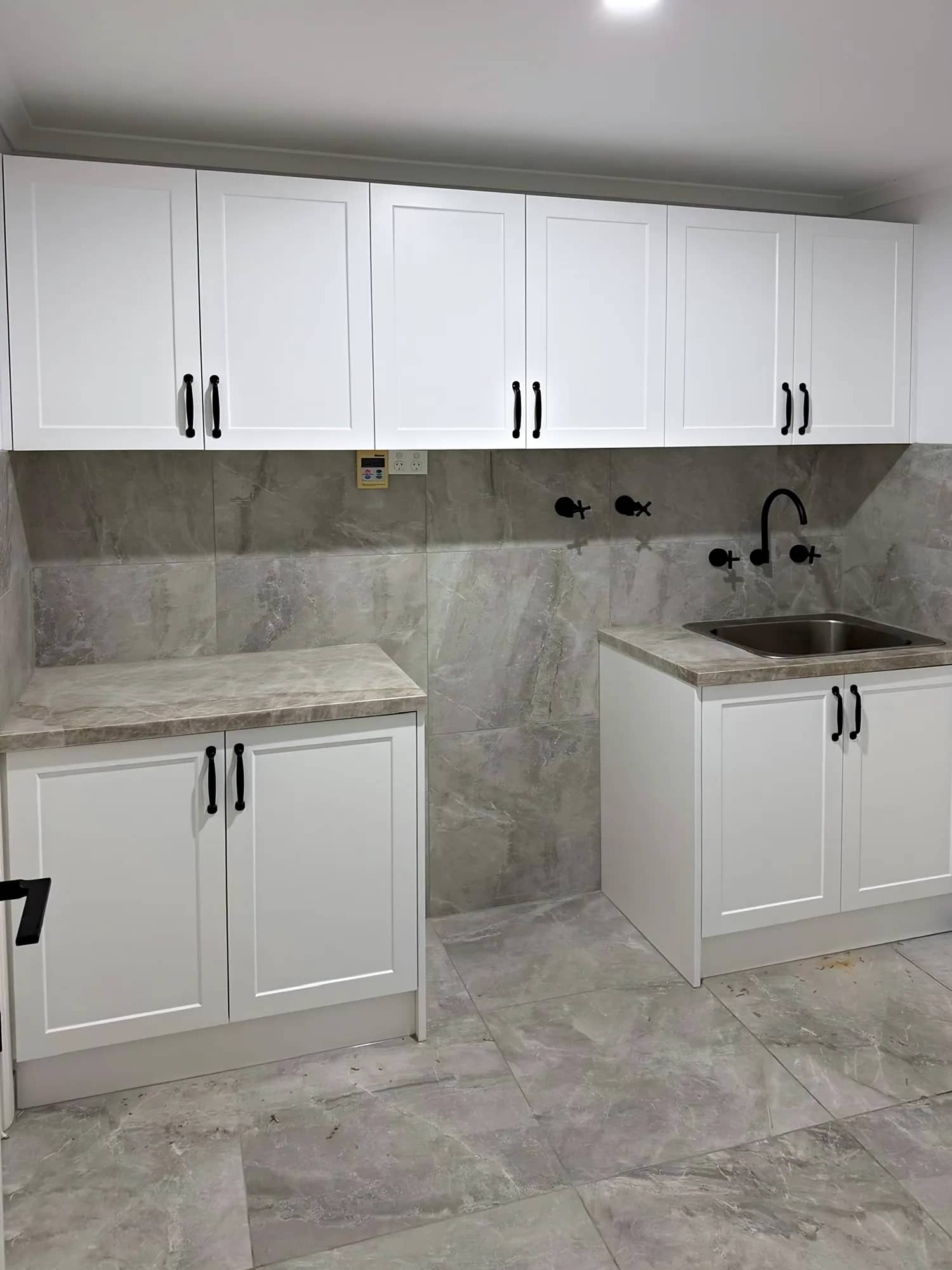 Laundry with white shaker-style cabinets, black handles and grey stone-look splashback and floor tiles