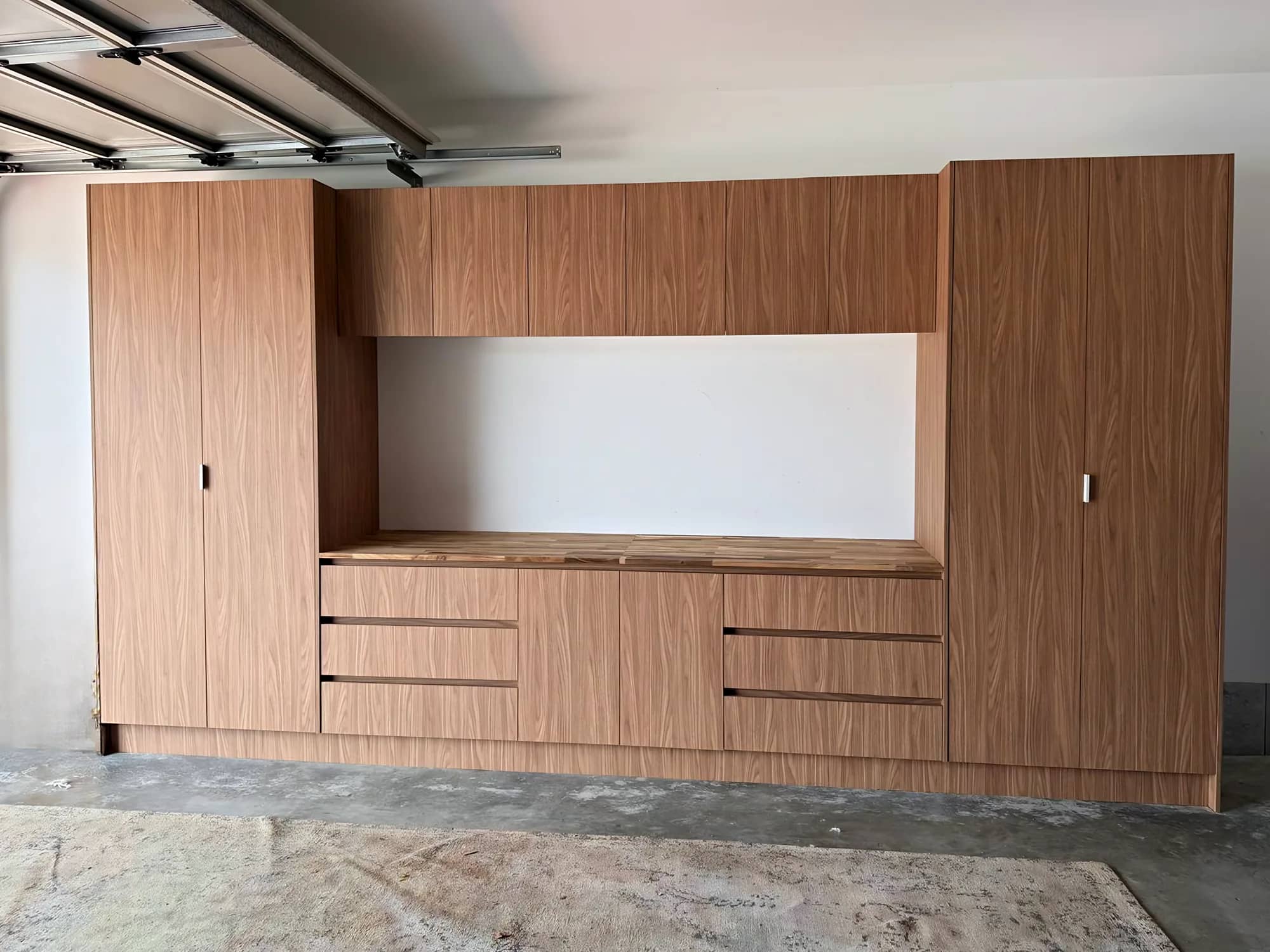 Garage storage wall with tall walnut-look cabinets and a timber benchtop