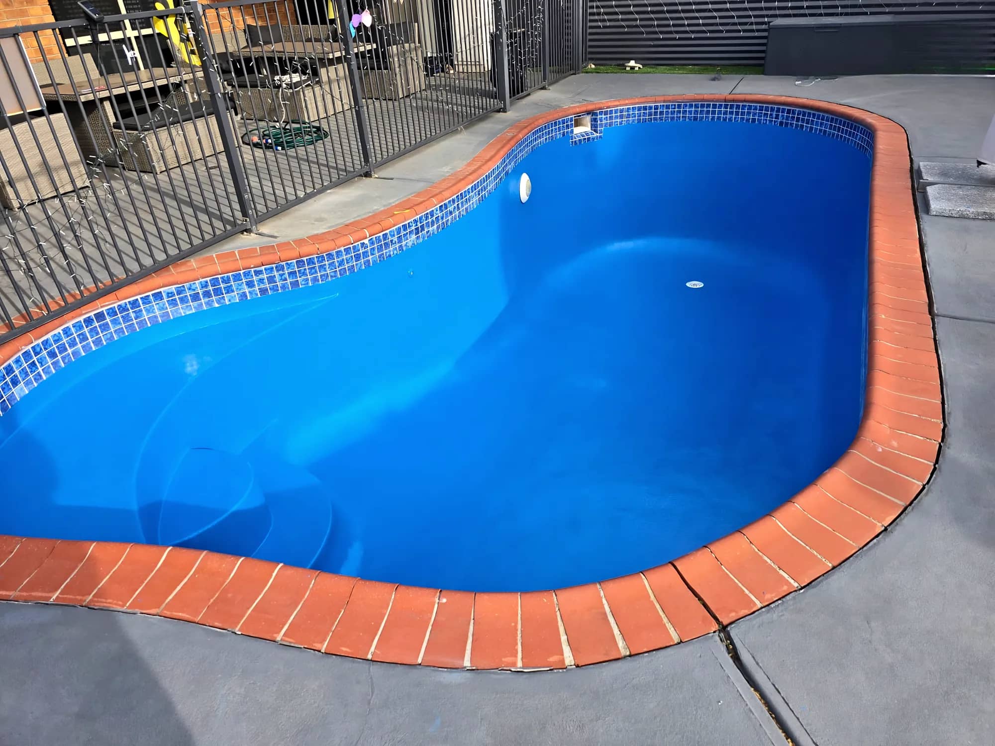 Close-up of a blue painted pool with blue mosaic waterline tiles and terracotta coping
