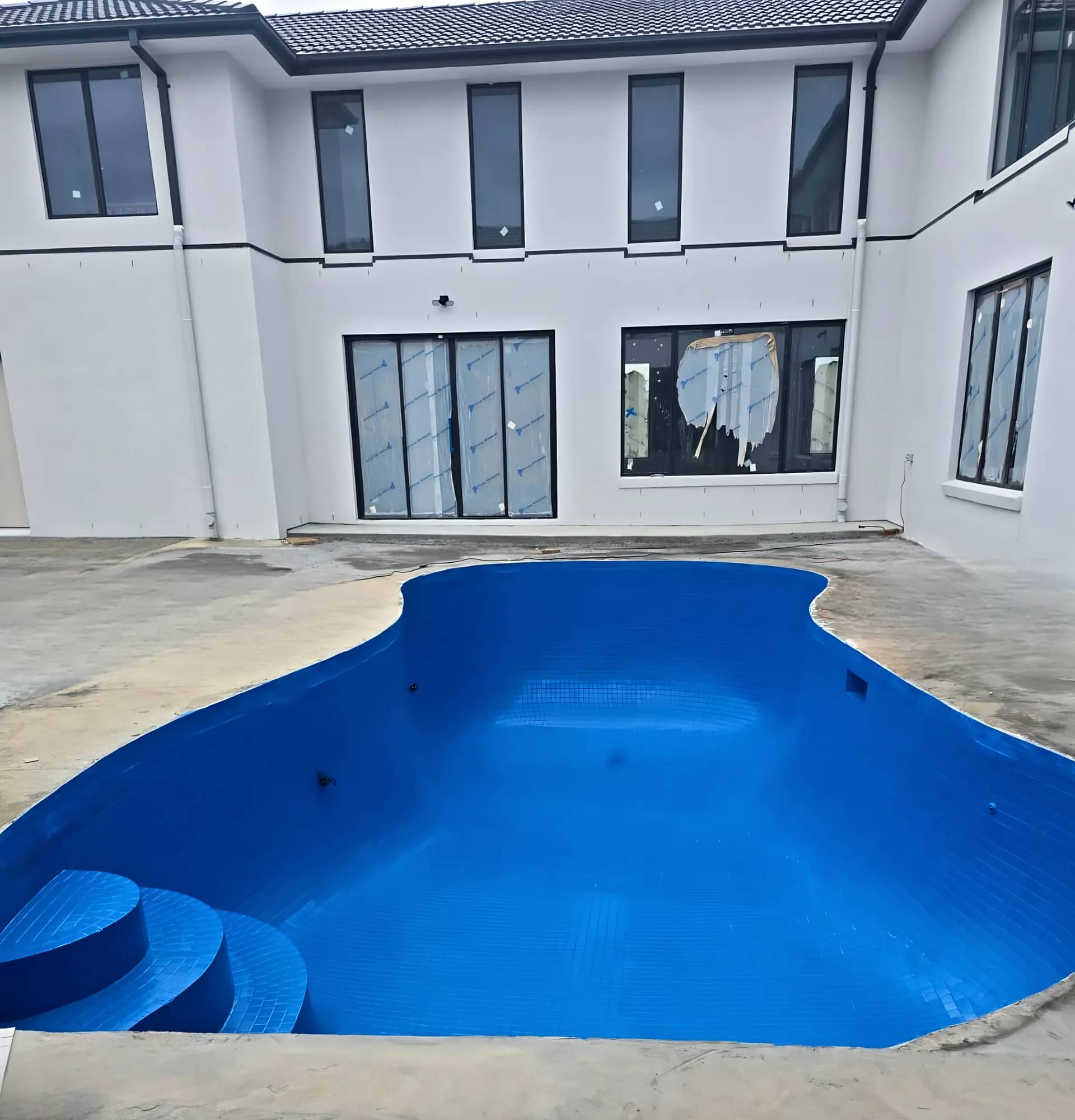 Blue mosaic-tiled swimming pool with wide entry steps in front of a new two-storey house