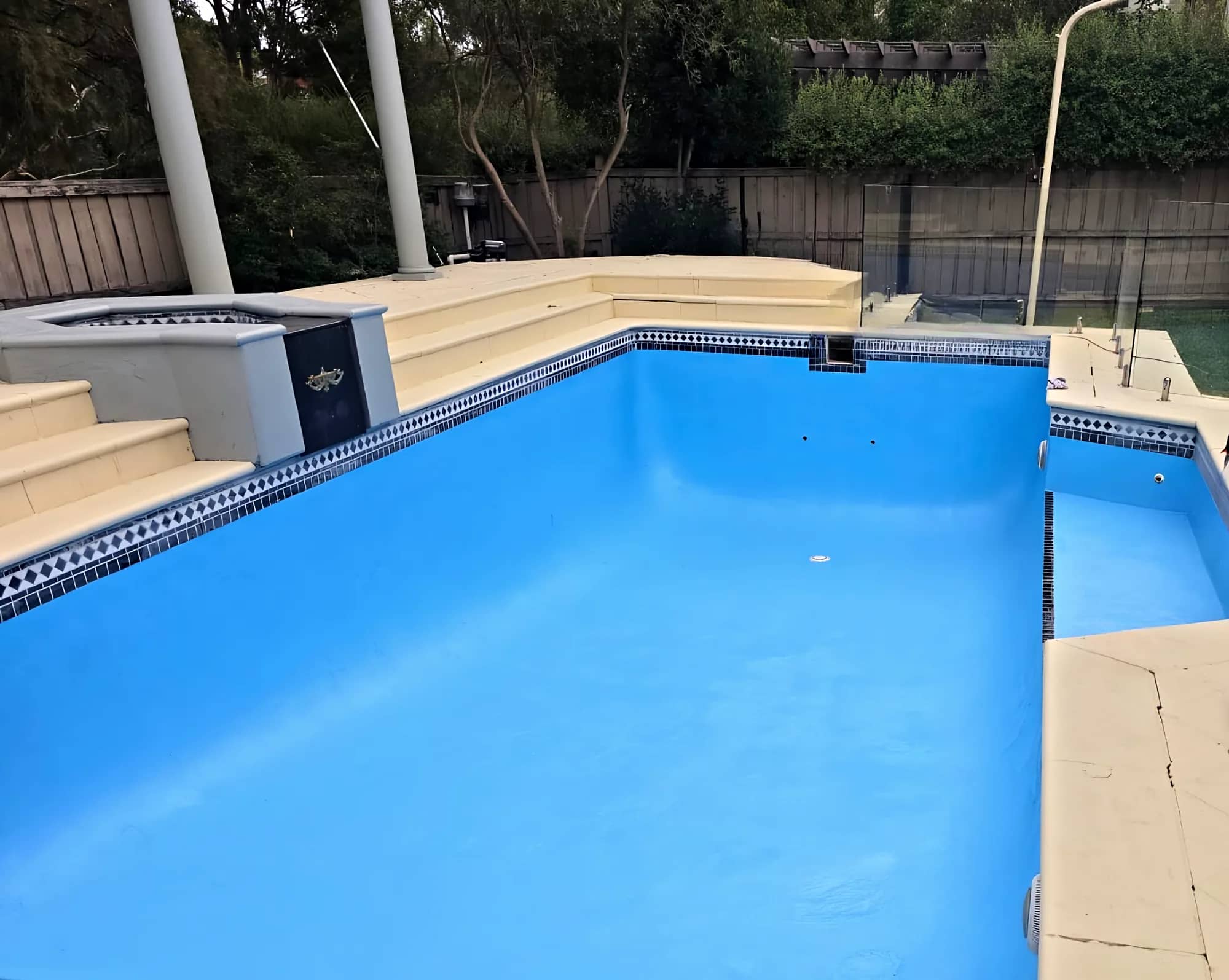 Pale-blue resurfaced pool with a frameless glass fence and sandstone coping