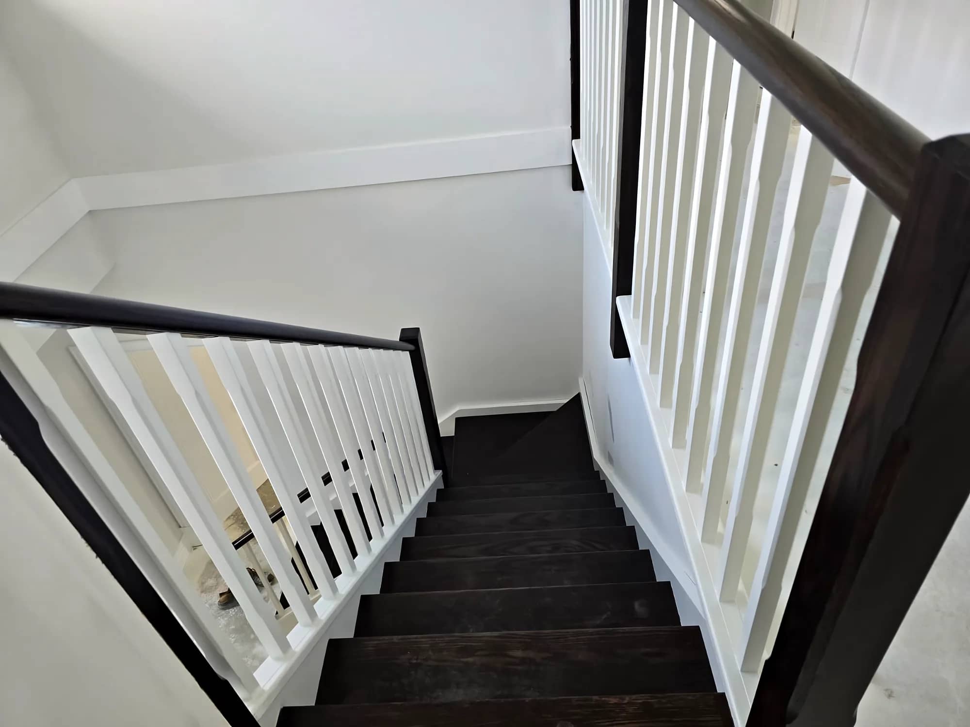 View down a staircase with white balusters, a dark-stained handrail and dark-stained treads