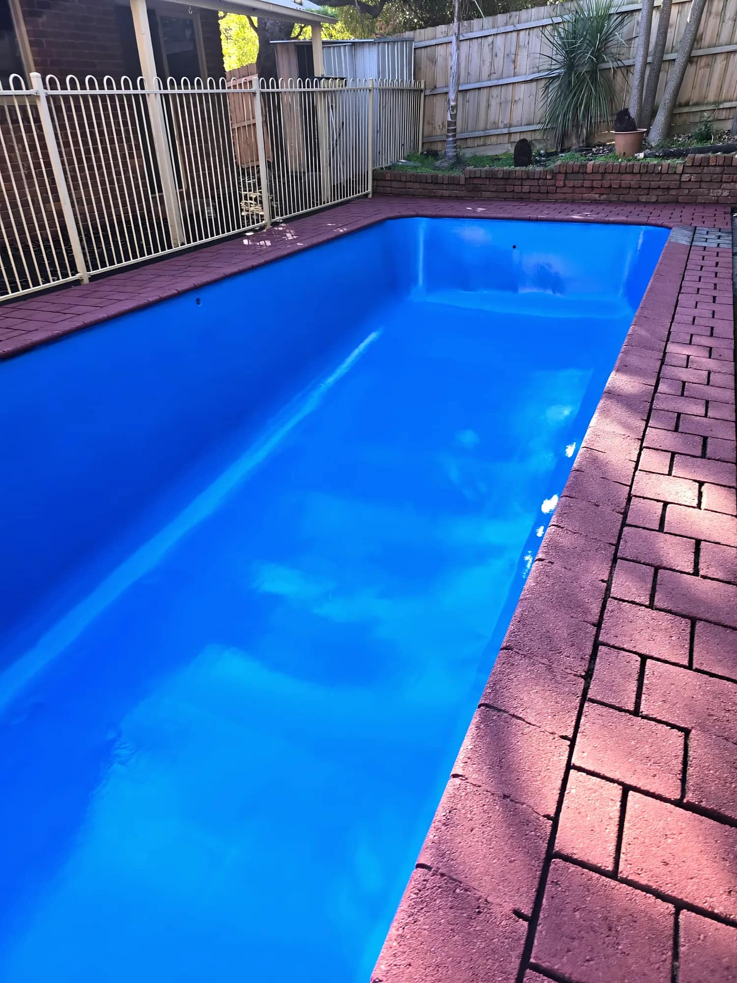After: Length view of a resurfaced pool with a gloss-blue finish and red brick-paver coping