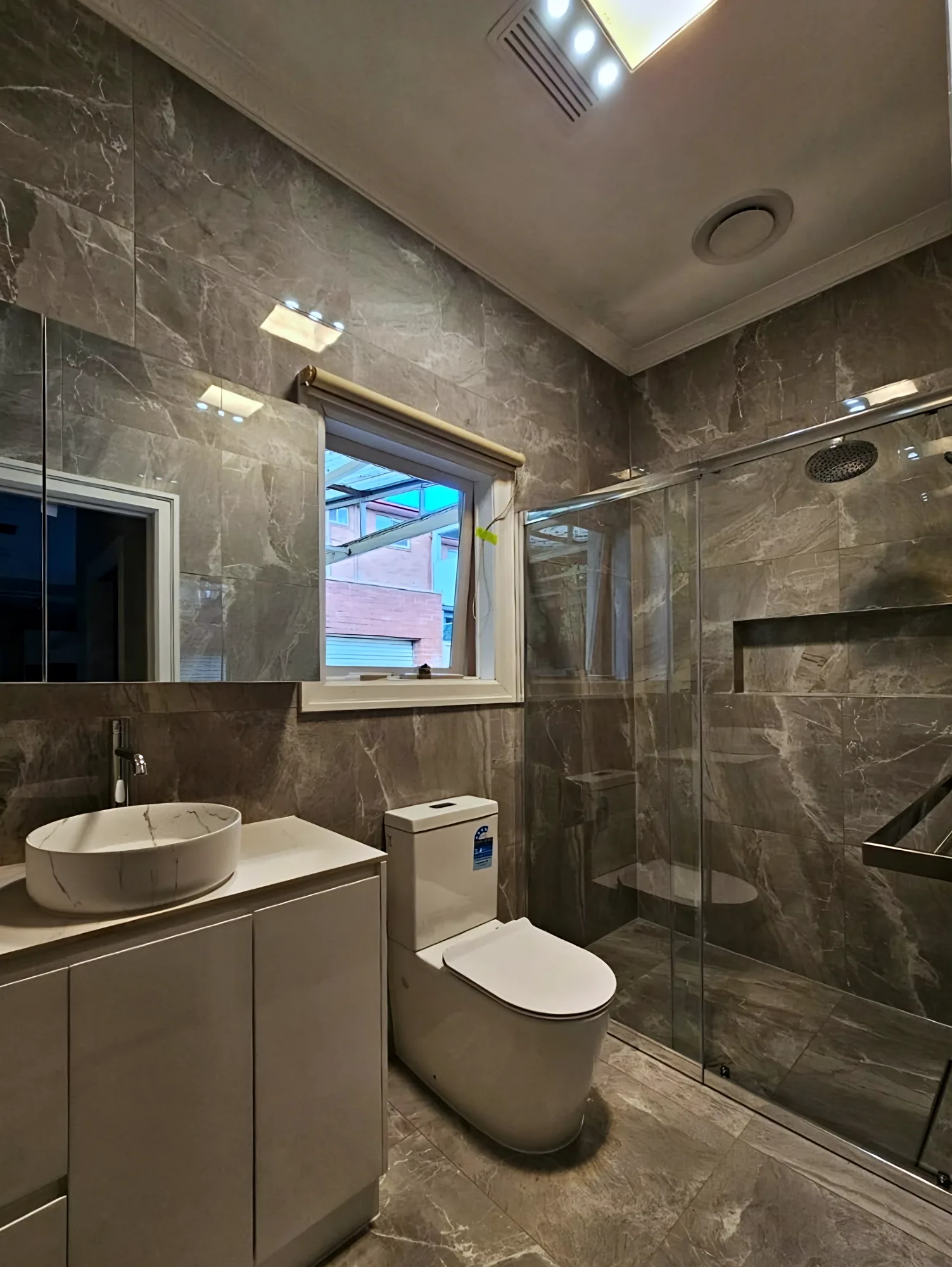 Bathroom with dark stone-look wall and floor tiles, a vessel basin and a frameless glass shower