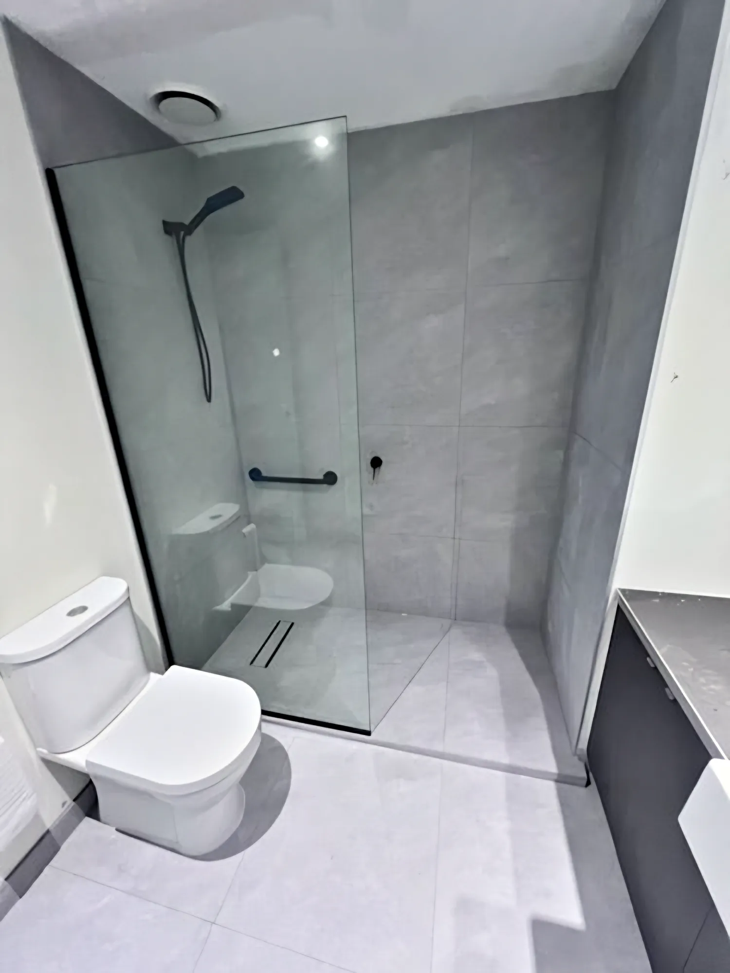 Walk-in shower with grey wall and floor tiles and a fixed glass panel