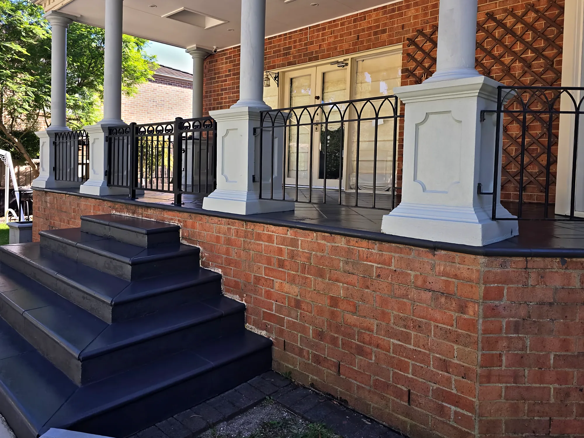 Brick verandah with charcoal-coated steps and deck edge, white columns and a black metal balustrade