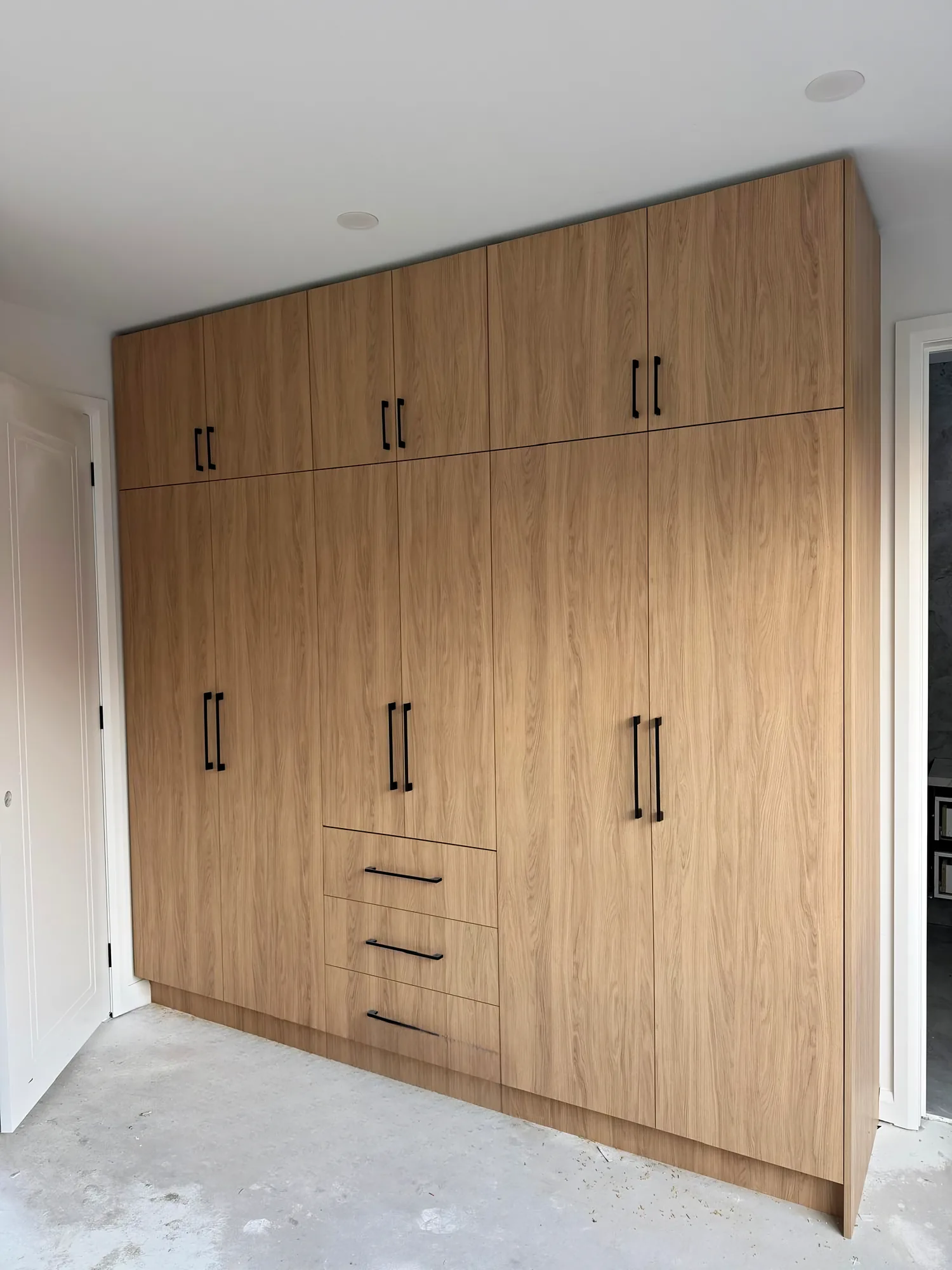 Full-height built-in wardrobe with oak-look doors and black handles
