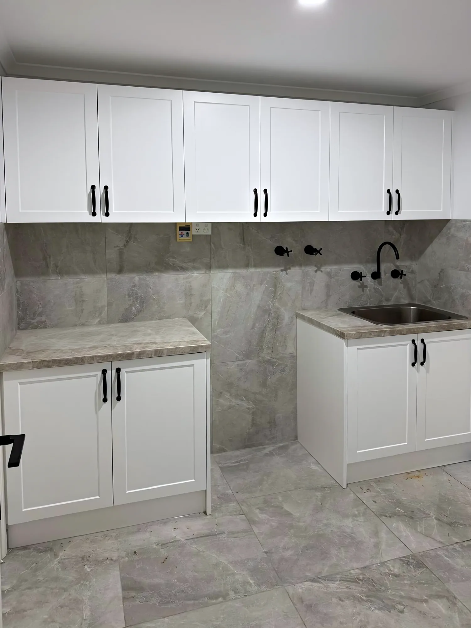 Laundry with white shaker-style cabinets, black handles and grey stone-look splashback and floor tiles