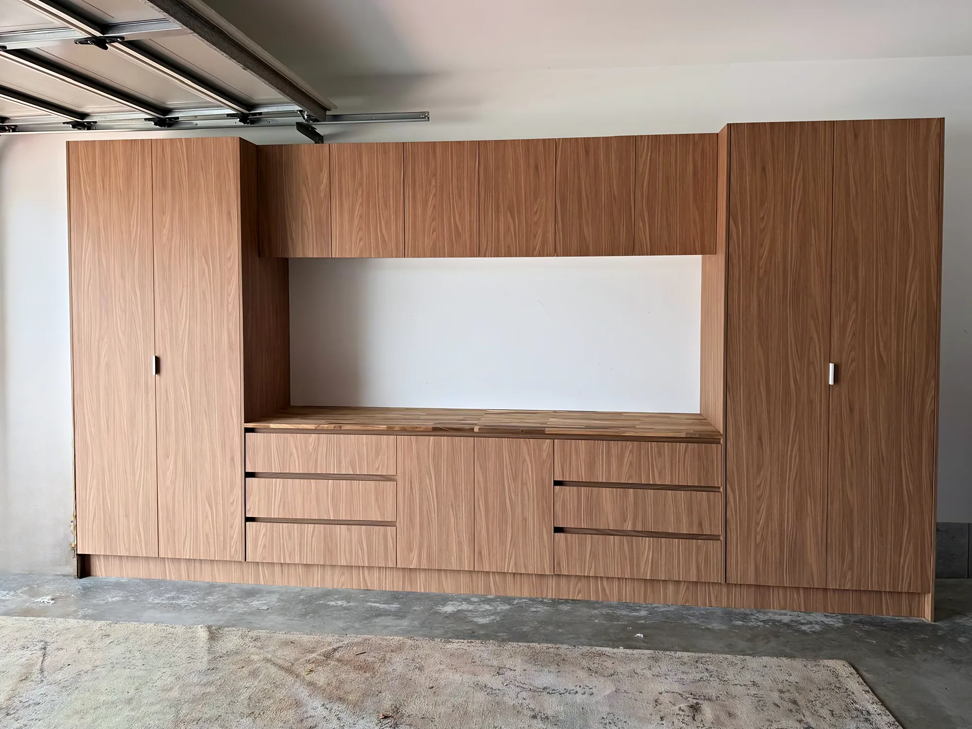 Garage storage wall with tall walnut-look cabinets and a timber benchtop