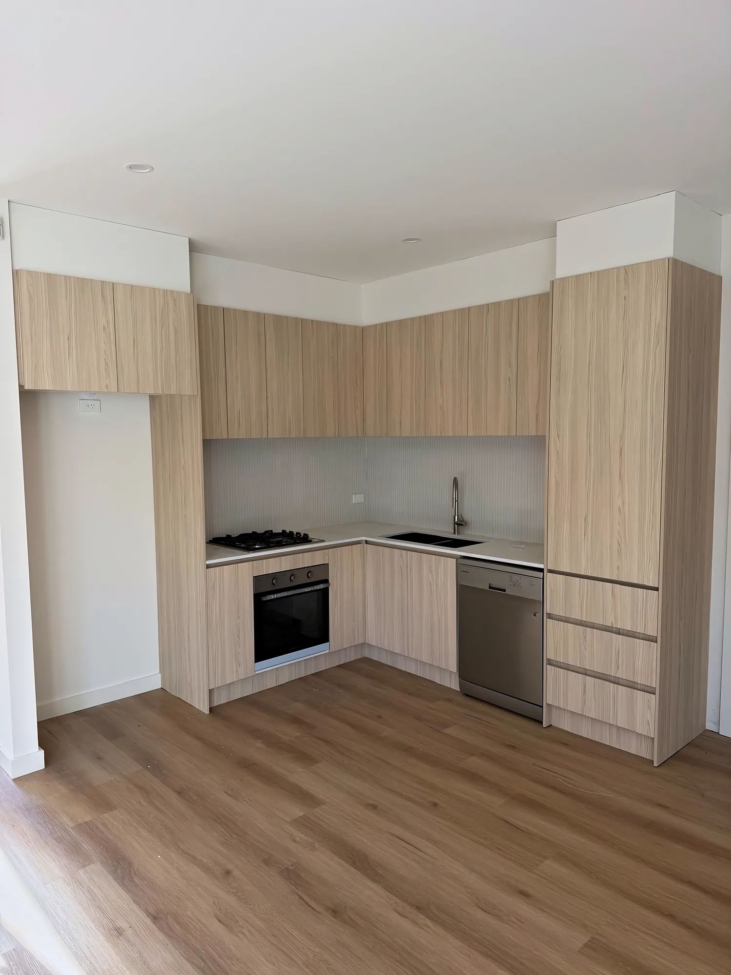 L-shaped kitchen with light oak-look cabinetry, a white benchtop and a fluted splashback
