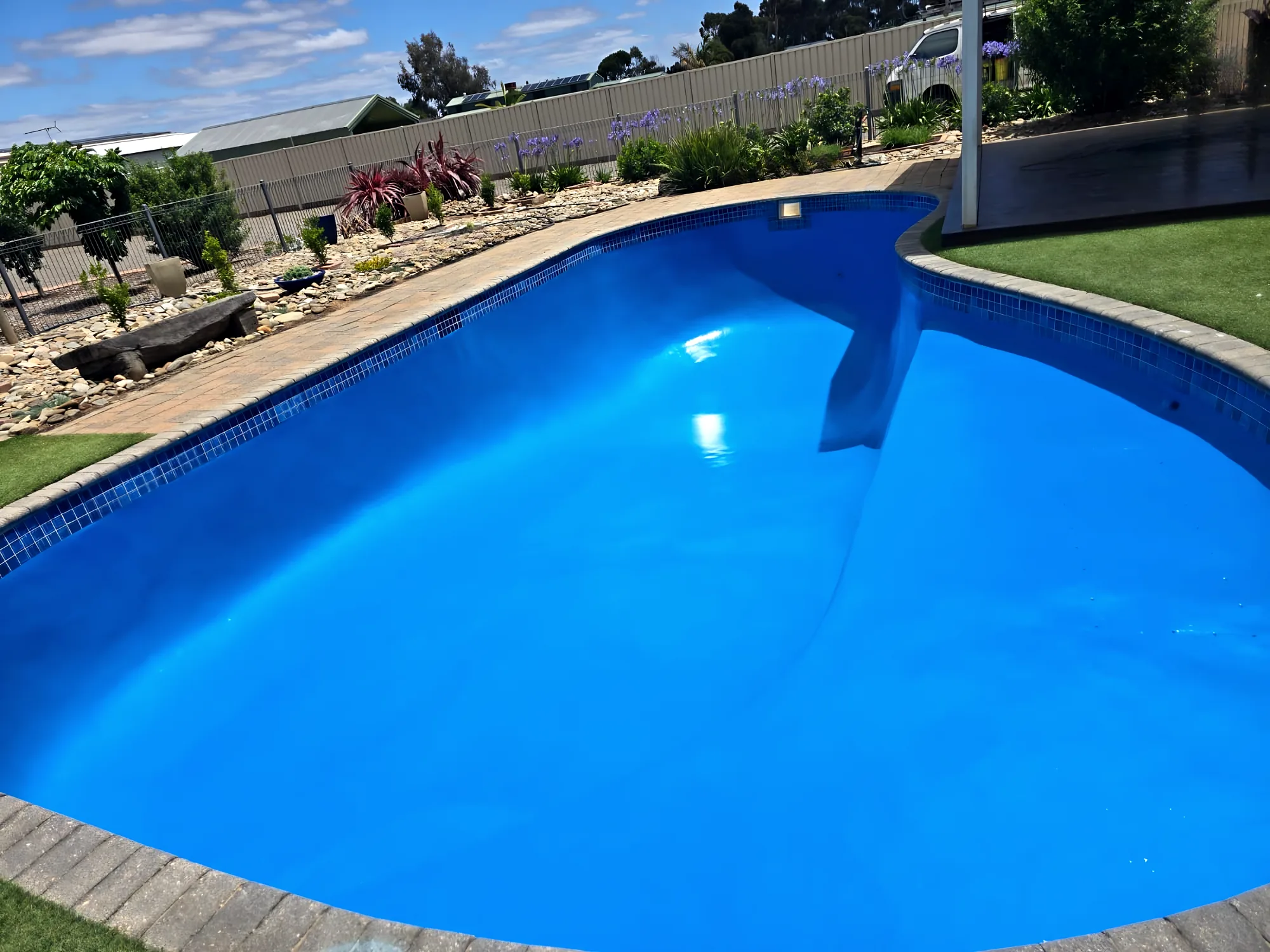 Close view of a glossy blue resurfaced pool with a waterline tile band and garden behind