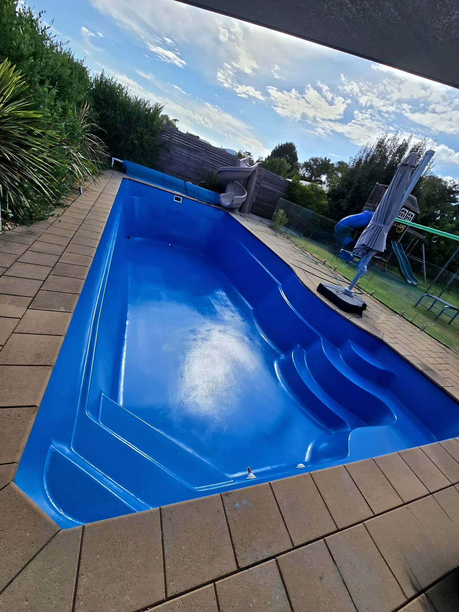 Rectangular fibreglass pool with entry steps and sandstone pavers after recoating, under an open sky