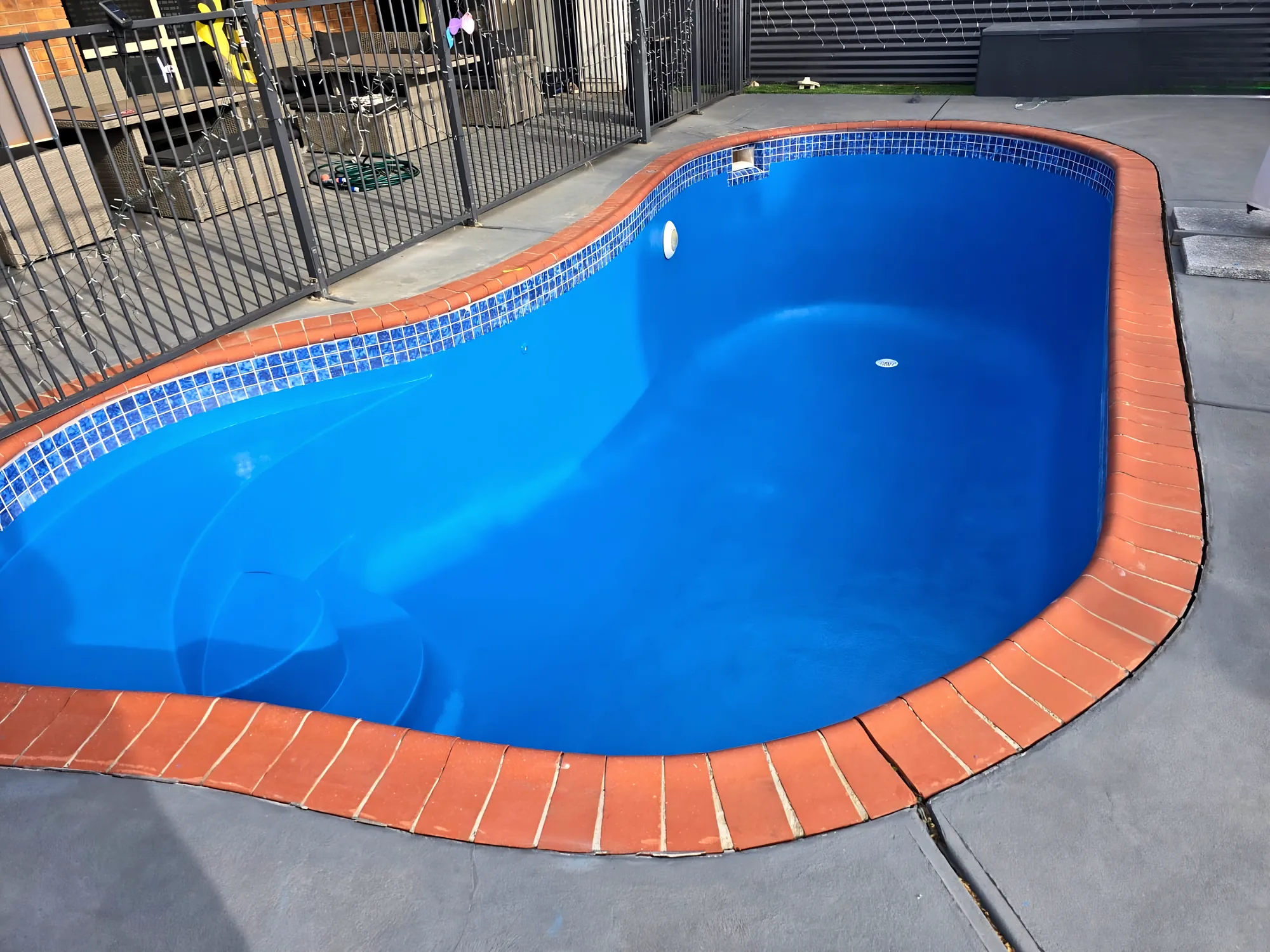 Close-up of a blue painted pool with blue mosaic waterline tiles and terracotta coping