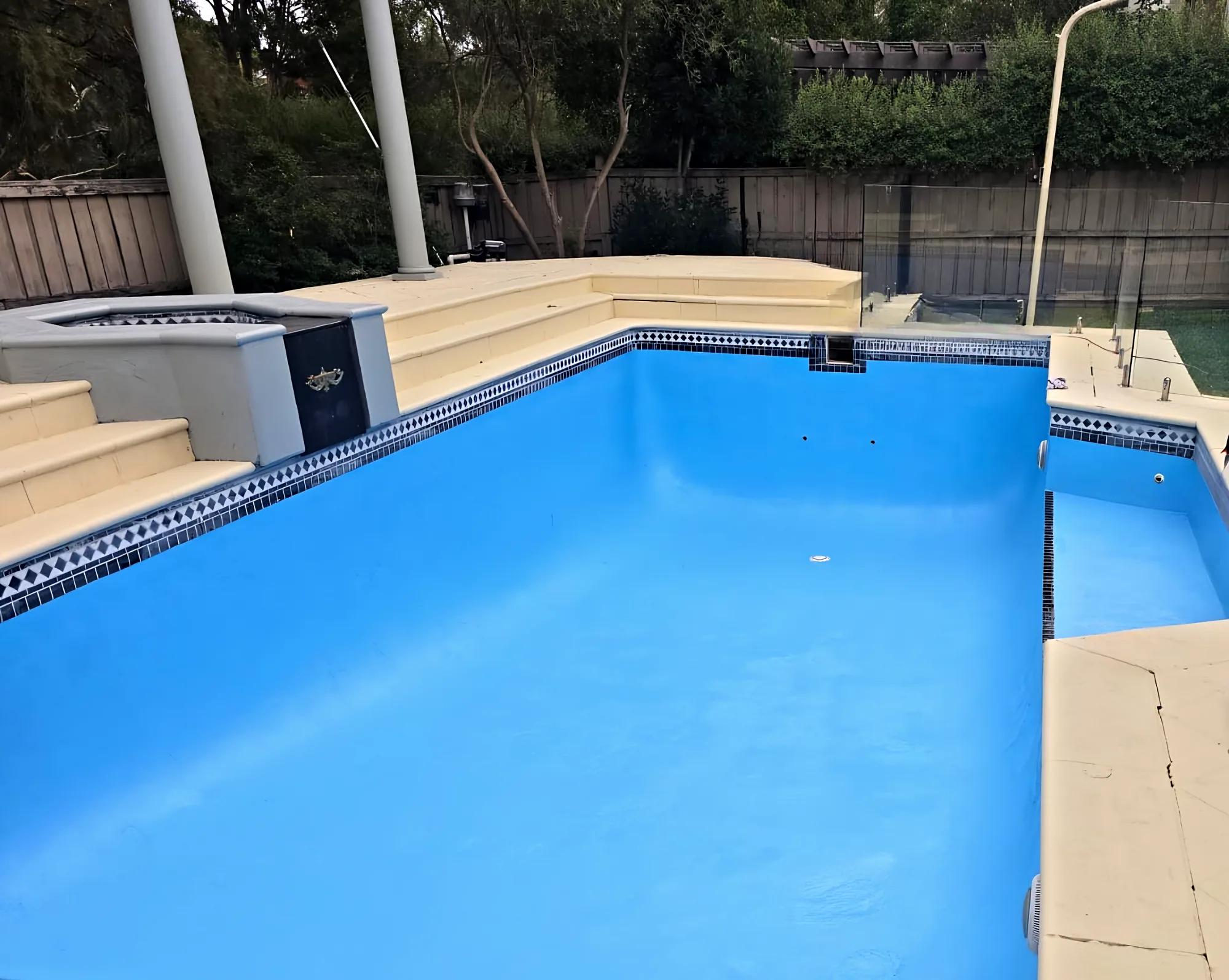 Pale-blue resurfaced pool with a frameless glass fence and sandstone coping
