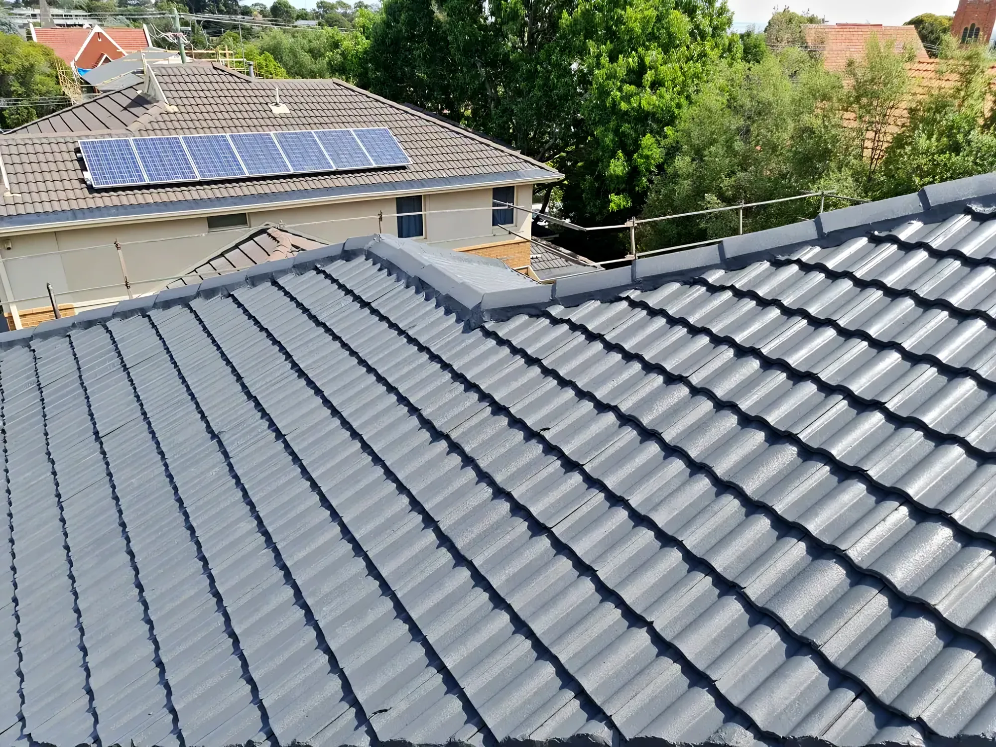 Concrete tile roof freshly restored in grey with crisp ridge capping, suburban rooftops beyond