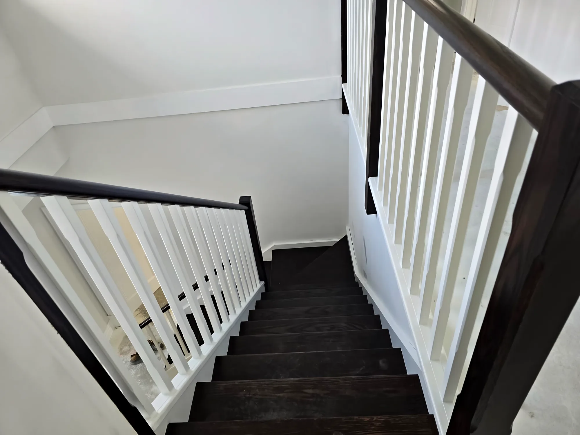 View down a staircase with white balusters, a dark-stained handrail and dark-stained treads